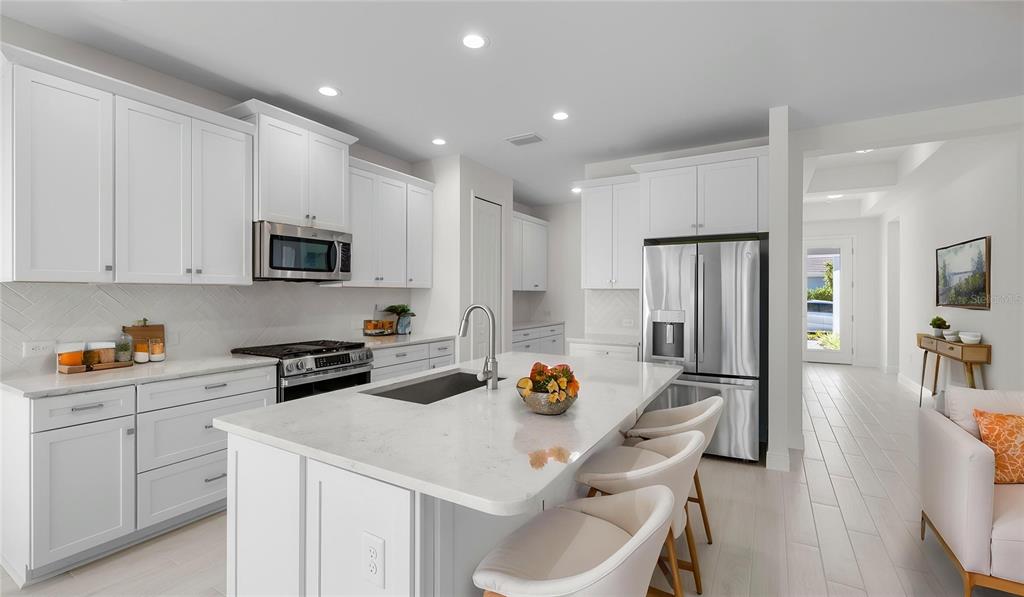A modern white kitchen features a large quartz island, stainless steel appliances, and light flooring — 13411 HERITAGE PRESERVE DRIVE, FORT MYERS, FL