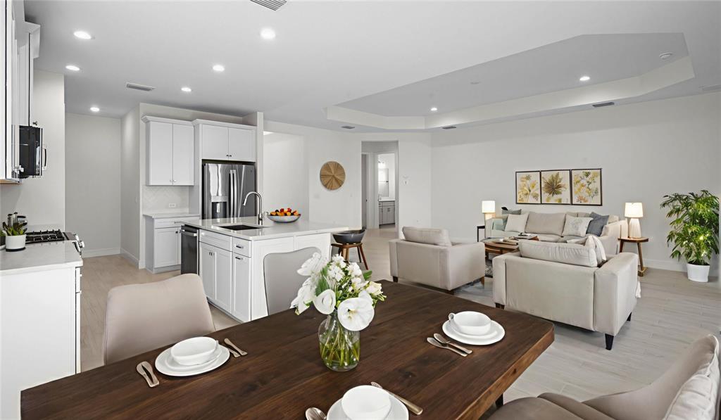 An open-concept kitchen, dining area, and living room featuring white cabinetry and light flooring — 13411 HERITAGE PRESERVE DRIVE, FORT MYERS, FL