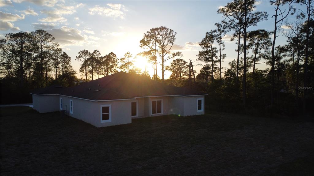 An aerial view of the back of a single-story house at sunset with trees — 5245 PEBBLE BEACH DRIVE, SEBRING, FL
