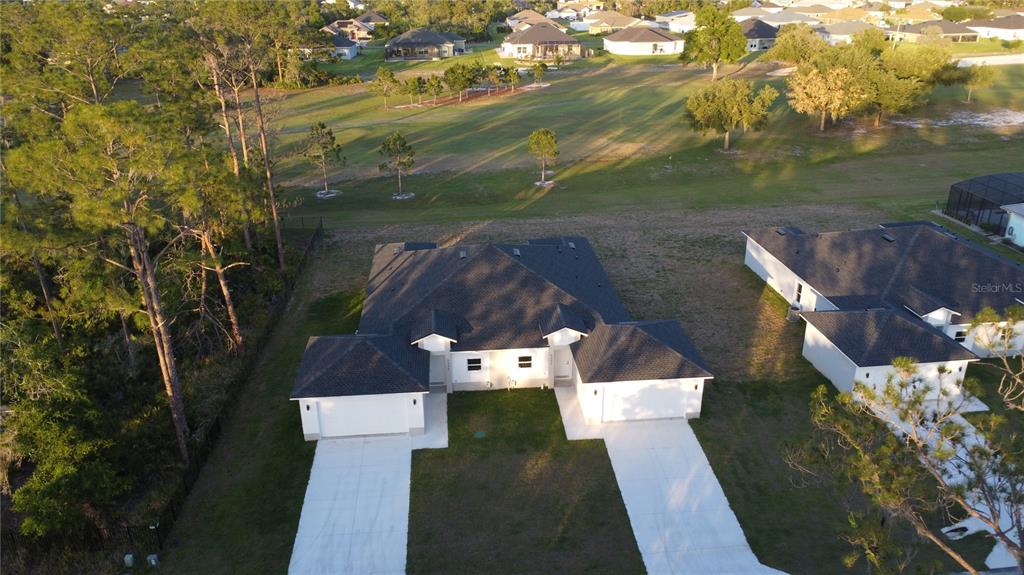 An aerial view shows a duplex with two garages and driveways facing a grassy field — 5245 PEBBLE BEACH DRIVE, SEBRING, FL