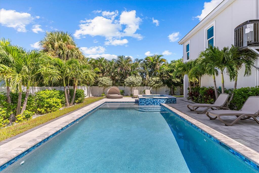 A backyard swimming pool with a spa, lounge chairs, and palm trees beside a house — 107 12TH STREET, BELLEAIR BEACH, FL