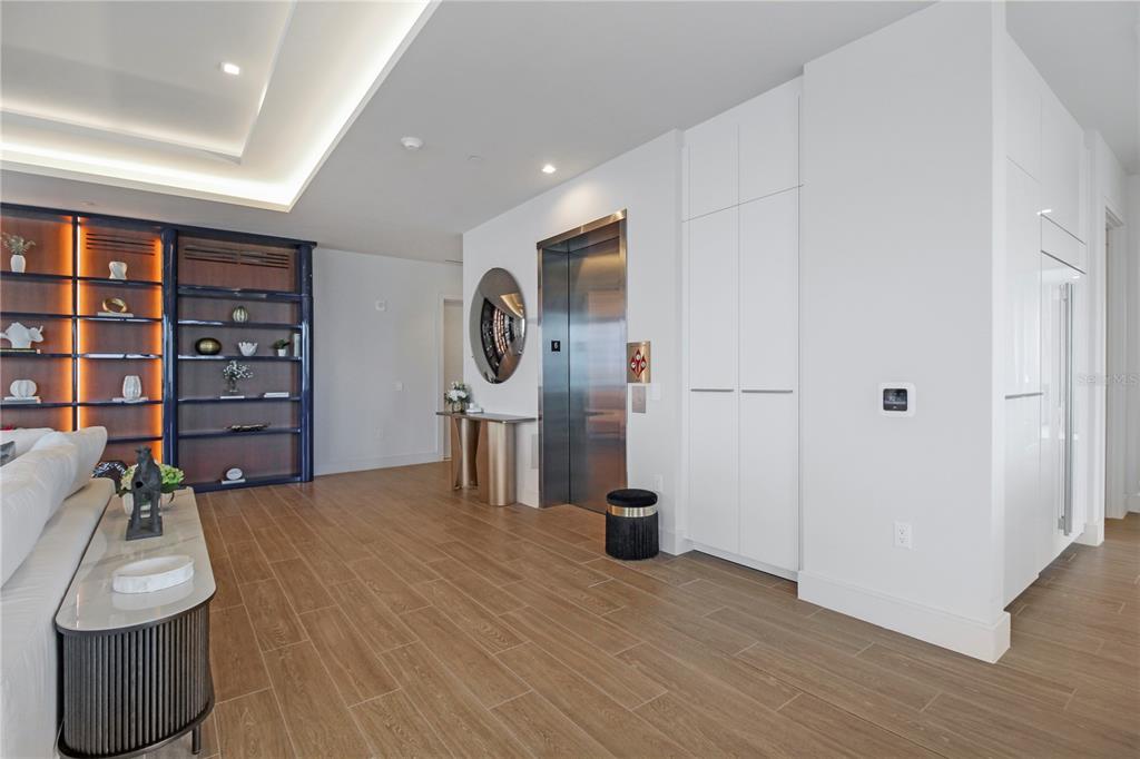 A spacious living room features white sectional sofas, wood-look tile floors, and a large display shelf — 1591 GULF OF MEXICO DRIVE UNIT 619, LONGBOAT KEY, FL