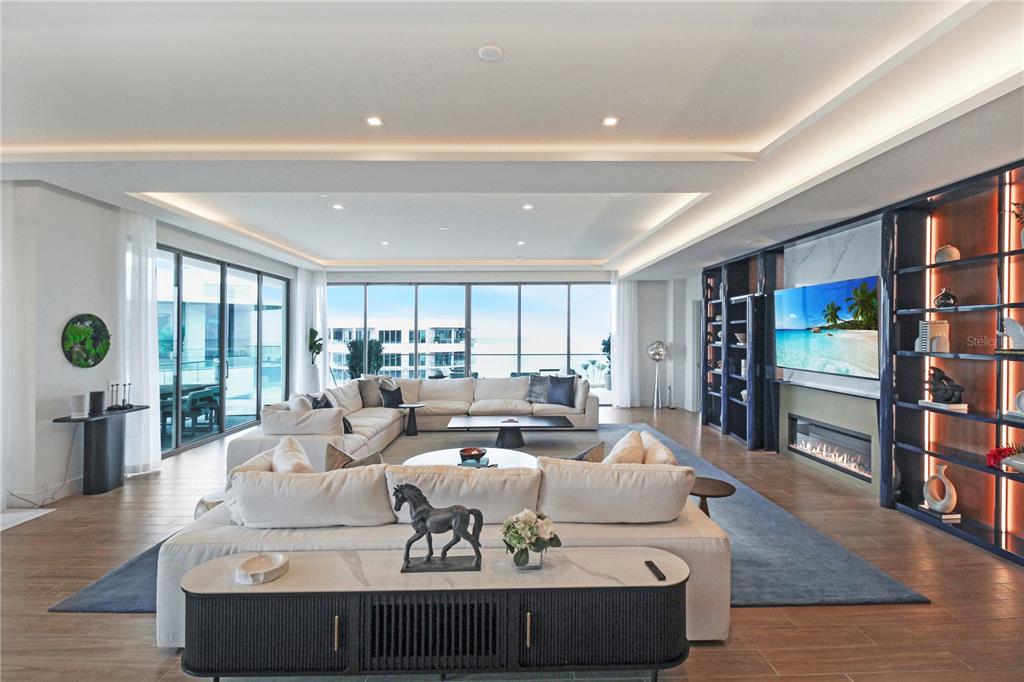 A modern living area features wood-look tile flooring, a built-in bookshelf, and a private elevator — 1591 GULF OF MEXICO DRIVE UNIT 619, LONGBOAT KEY, FL