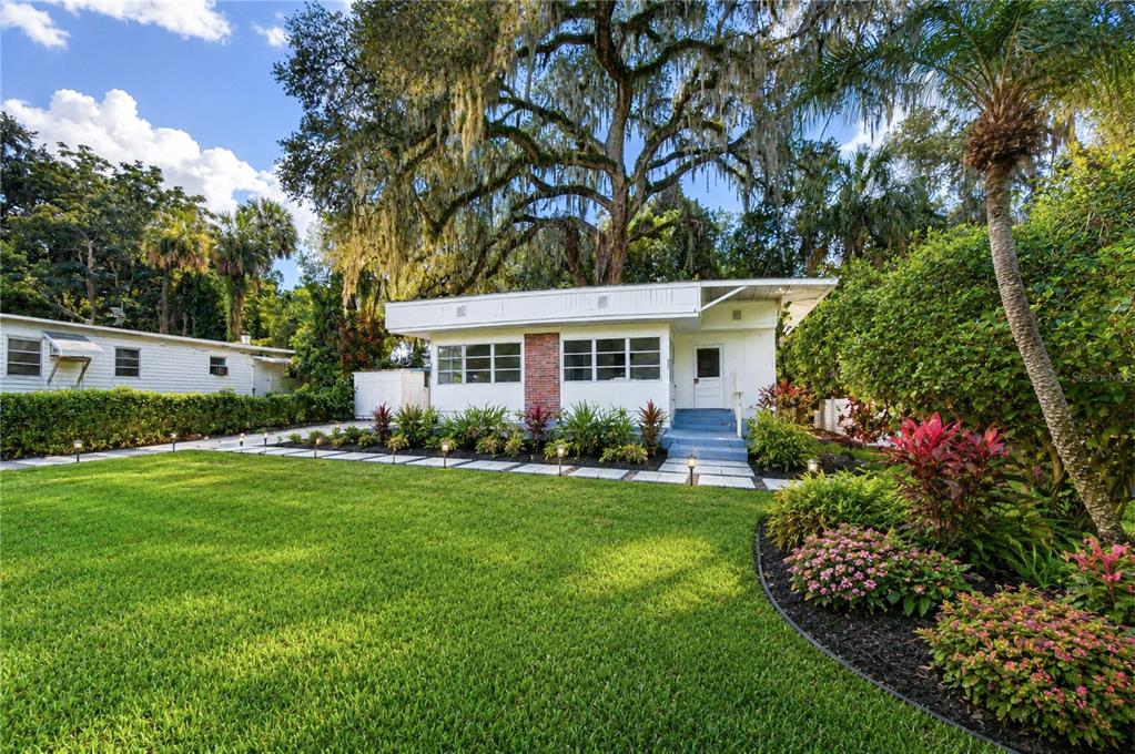 A white single-story house with a brick accent wall sits behind a manicured green lawn — 39200 FIBELKORN ROAD, ZEPHYRHILLS, FL