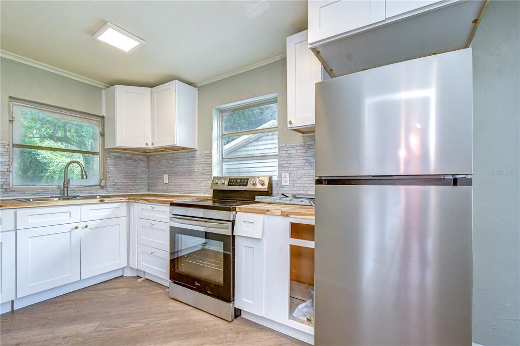 A kitchen features white cabinets, stainless steel appliances, a wood countertop, and a tiled backsplash — 39200 FIBELKORN ROAD, ZEPHYRHILLS, FL