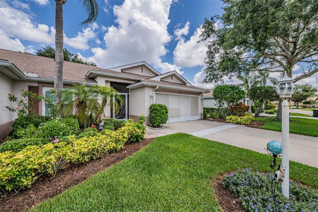 A single-story house with a beige exterior, a two-car garage, and a landscaped front yard — 1230 CORINTH GREENS DRIVE UNIT 2, SUN CITY CENTER, FL