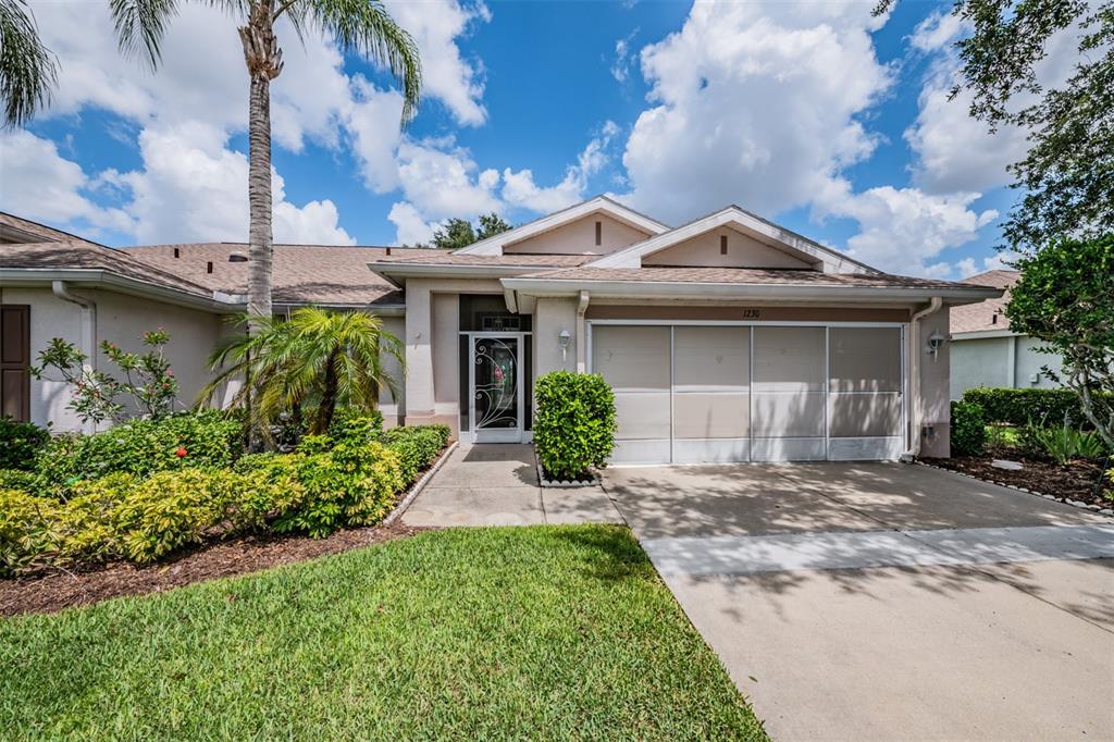 A single-story house with a beige exterior, a two-car garage, and a landscaped front yard — 1230 CORINTH GREENS DRIVE UNIT 2, SUN CITY CENTER, FL