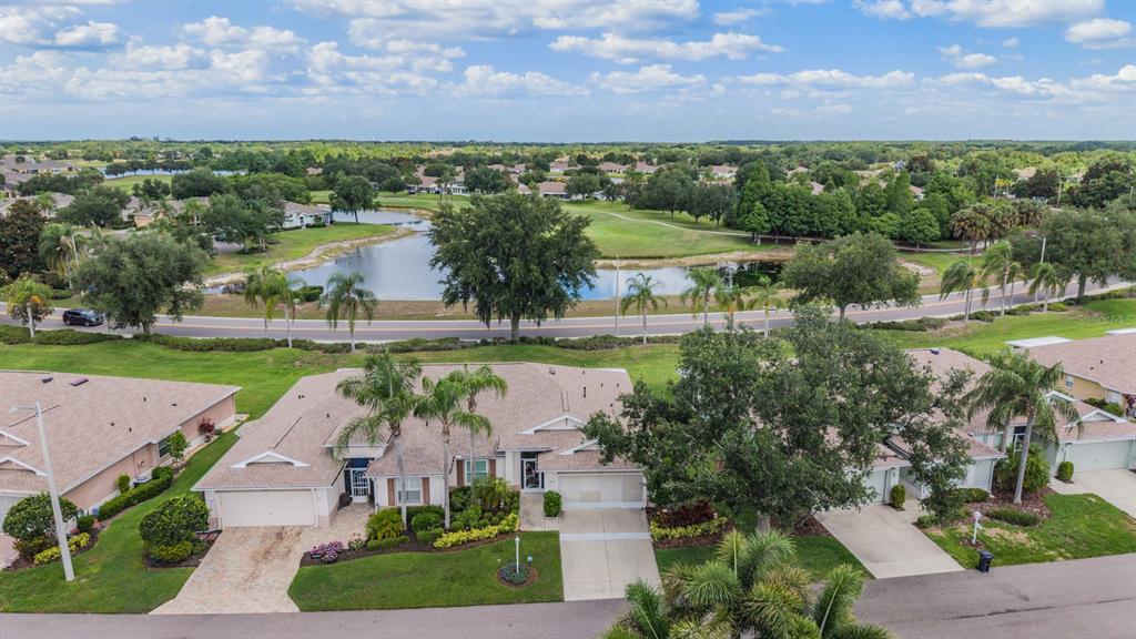 An aerial view shows a residential house with a driveway and palm trees near a pond — 1230 CORINTH GREENS DRIVE UNIT 2, SUN CITY CENTER, FL