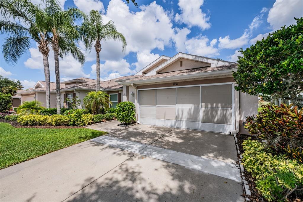 A single-story house exterior features a two-car garage with a screen door and palm trees — 1230 CORINTH GREENS DRIVE UNIT 2, SUN CITY CENTER, FL