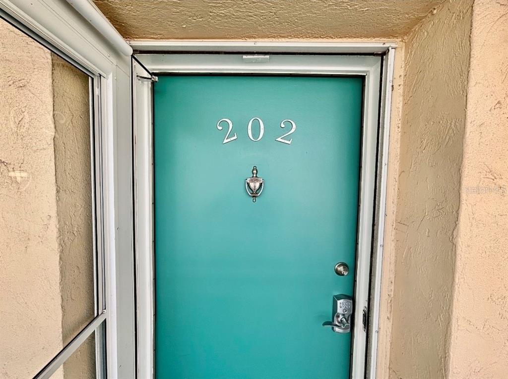 A teal front door with the number 202 and a silver knocker is set in a frame — 1215 S PORTOFINO DRIVE UNIT 202, SARASOTA, FL