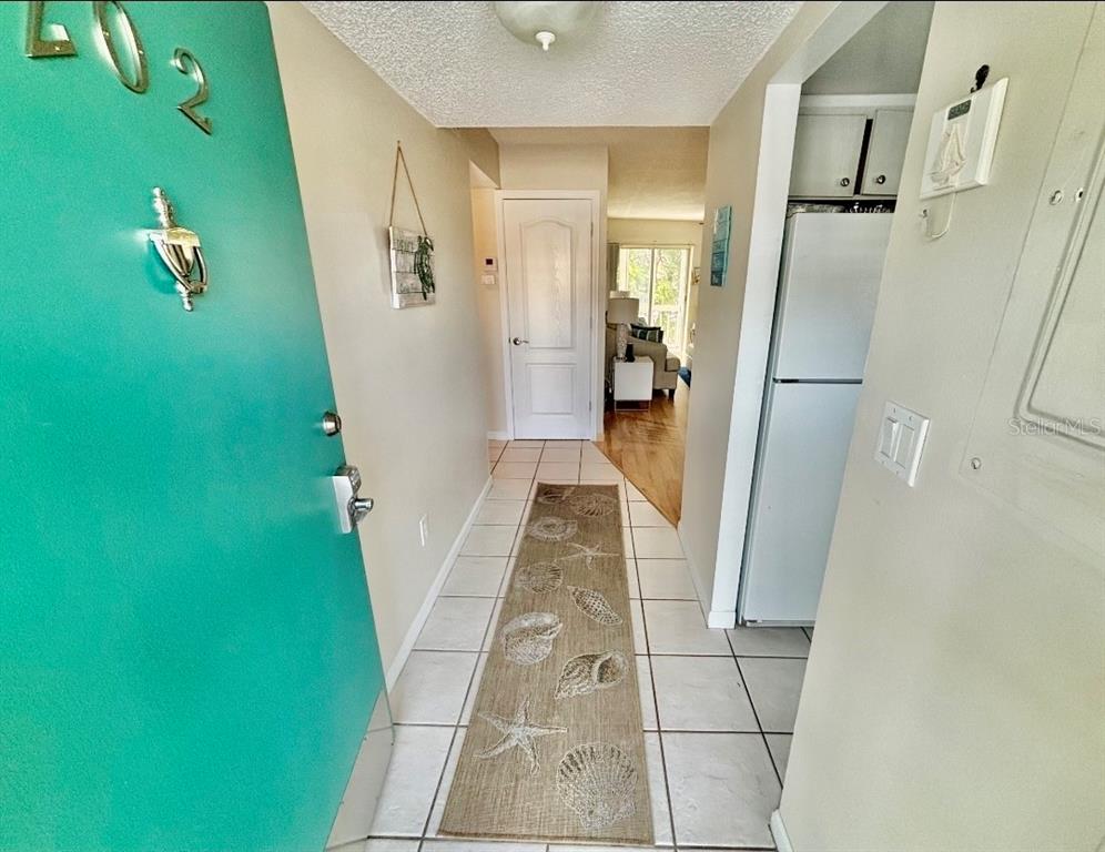 An entryway with a teal door, tiled floor, seashell runner, and a view into the living area — 1215 S PORTOFINO DRIVE UNIT 202, SARASOTA, FL