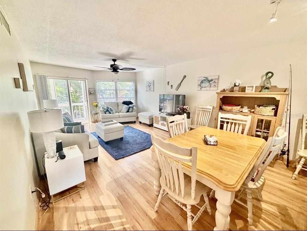 A living and dining area features light wood flooring, a ceiling fan, and coastal decor — 1215 S PORTOFINO DRIVE UNIT 202, SARASOTA, FL