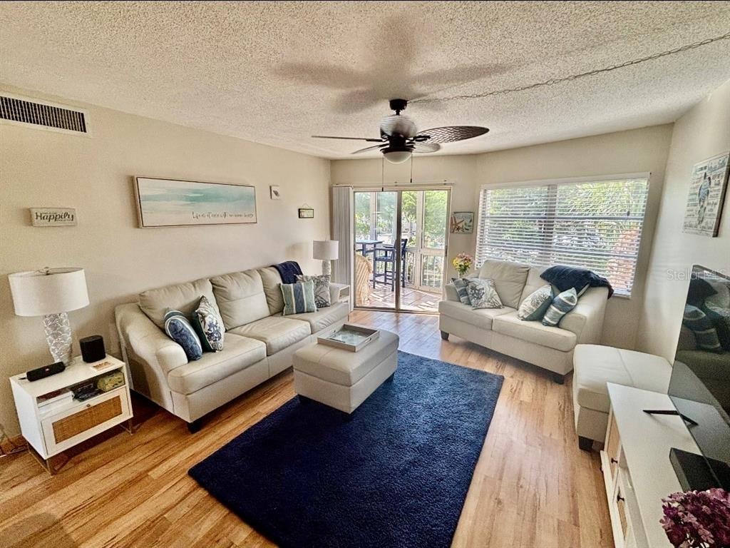A living room features a beige sofa and loveseat, a blue rug, and sliding glass doors — 1215 S PORTOFINO DRIVE UNIT 202, SARASOTA, FL