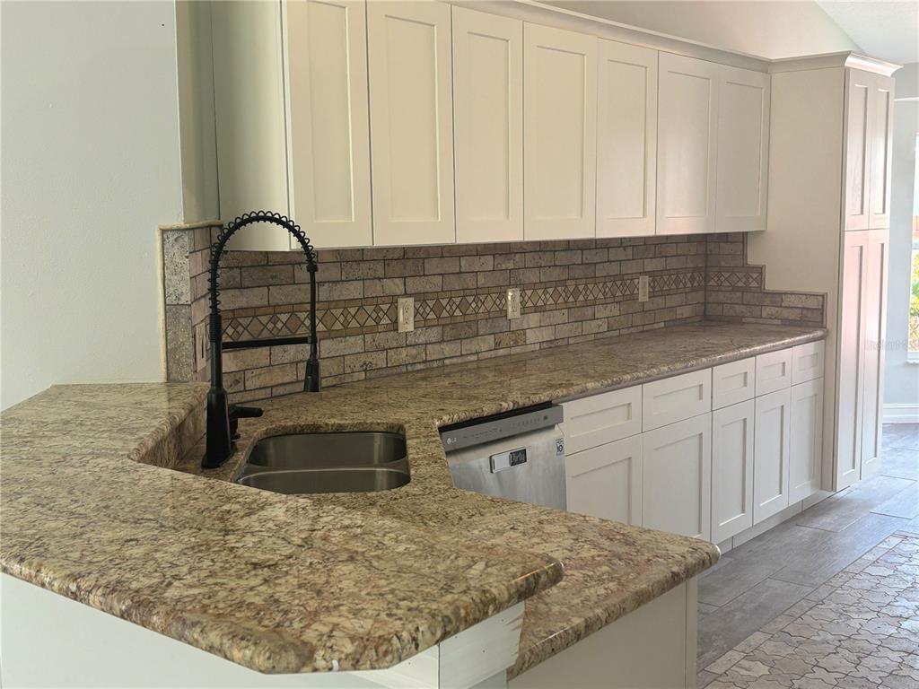 A kitchen features white shaker cabinets, granite countertops, a stainless steel dishwasher, and tiled backsplash — 2830 STRAND CIRCLE, OVIEDO, FL