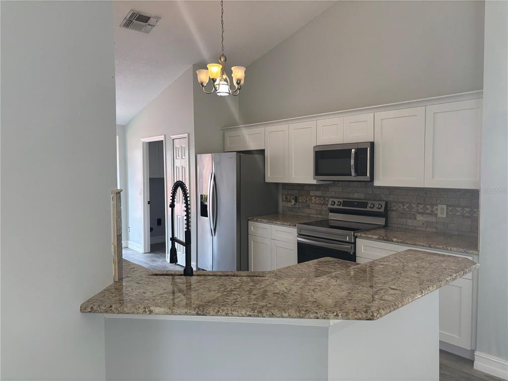 A kitchen features white cabinets, granite countertops, stainless steel appliances, and a breakfast bar — 2830 STRAND CIRCLE, OVIEDO, FL