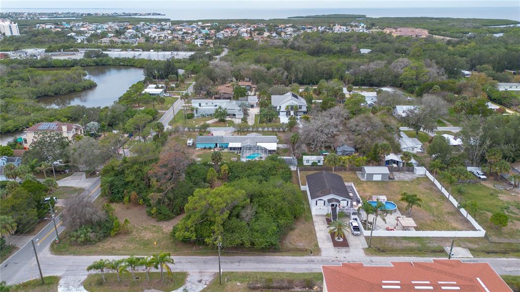 An aerial view shows residential houses with swimming pools and surrounding trees near a body of water — 6317 OELSNER STREET, NEW PORT RICHEY, FL