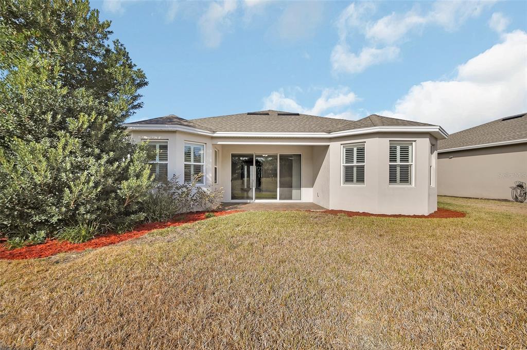 The rear exterior of a single-story house features a covered patio and a grassy yard — 509 ADENMORE TERRACE, DELAND, FL
