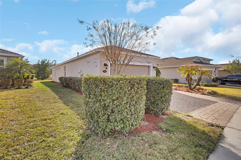 A beige house with a two-car garage, a paved driveway, and manicured hedges in front — 509 ADENMORE TERRACE, DELAND, FL