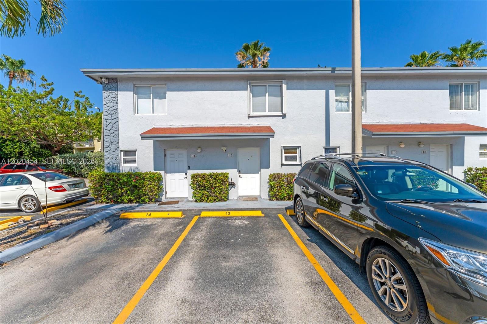 A two-story apartment building exterior features white stucco walls, red awnings, and numbered parking spaces — 8025 NW 8th St # 13, Miami FL 33126, MIAMI, FL