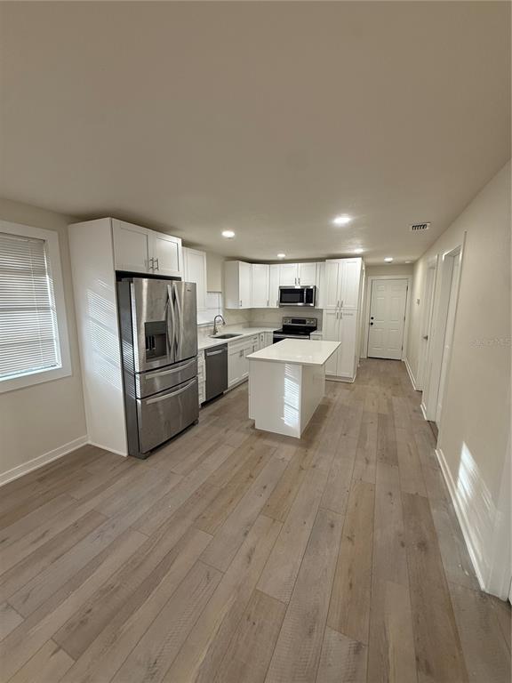 A kitchen features white cabinetry, stainless steel appliances, a center island, and light wood flooring — 14108 WILSON STREET, DADE CITY, FL