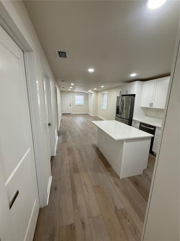 A kitchen with a white island and cabinets opens into a long, wood-floored living area — 14108 WILSON STREET, DADE CITY, FL