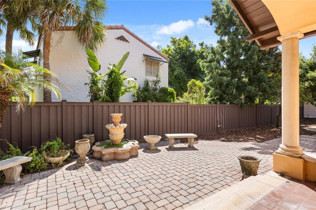 A paved patio features a stone fountain, benches, and planters against a brown privacy fence — 737 SPRINGDALE RD, ORLANDO, FL