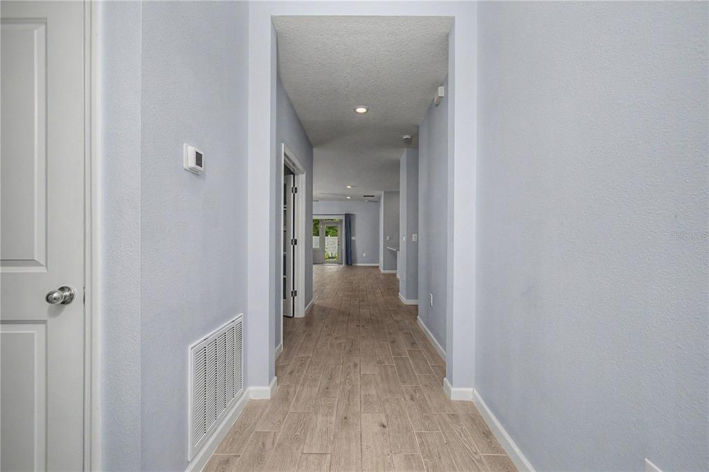 A hallway with light blue walls and wood-look tile flooring leads toward an open living area — 7795 SW 74TH LOOP, OCALA, FL
