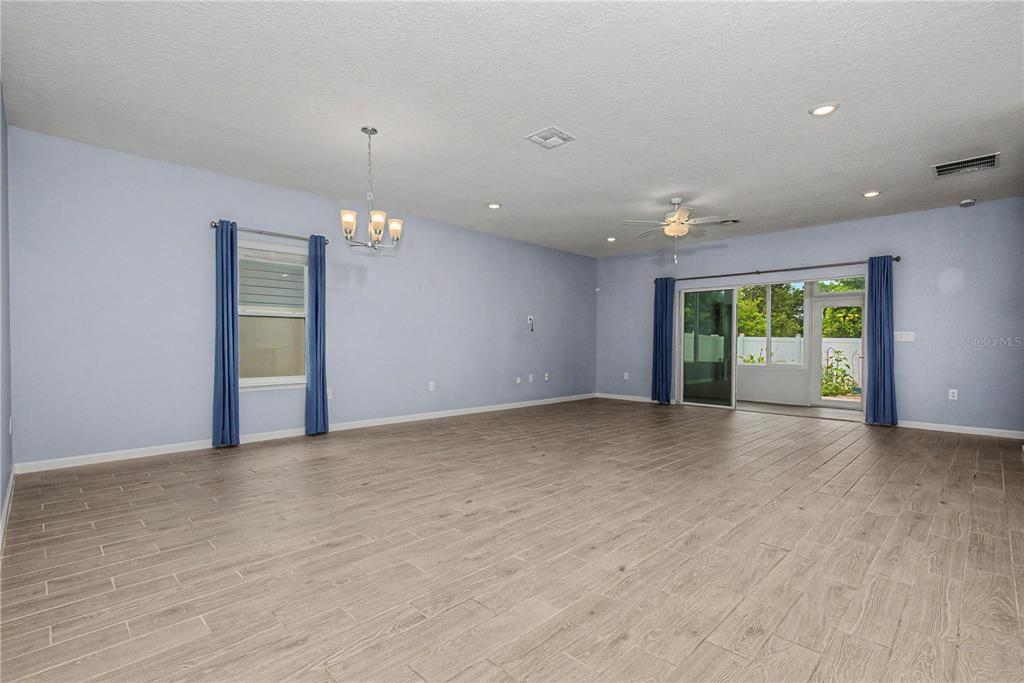 A spacious, light blue living room features wood-look tile flooring, a ceiling fan, and sliding doors — 7795 SW 74TH LOOP, OCALA, FL