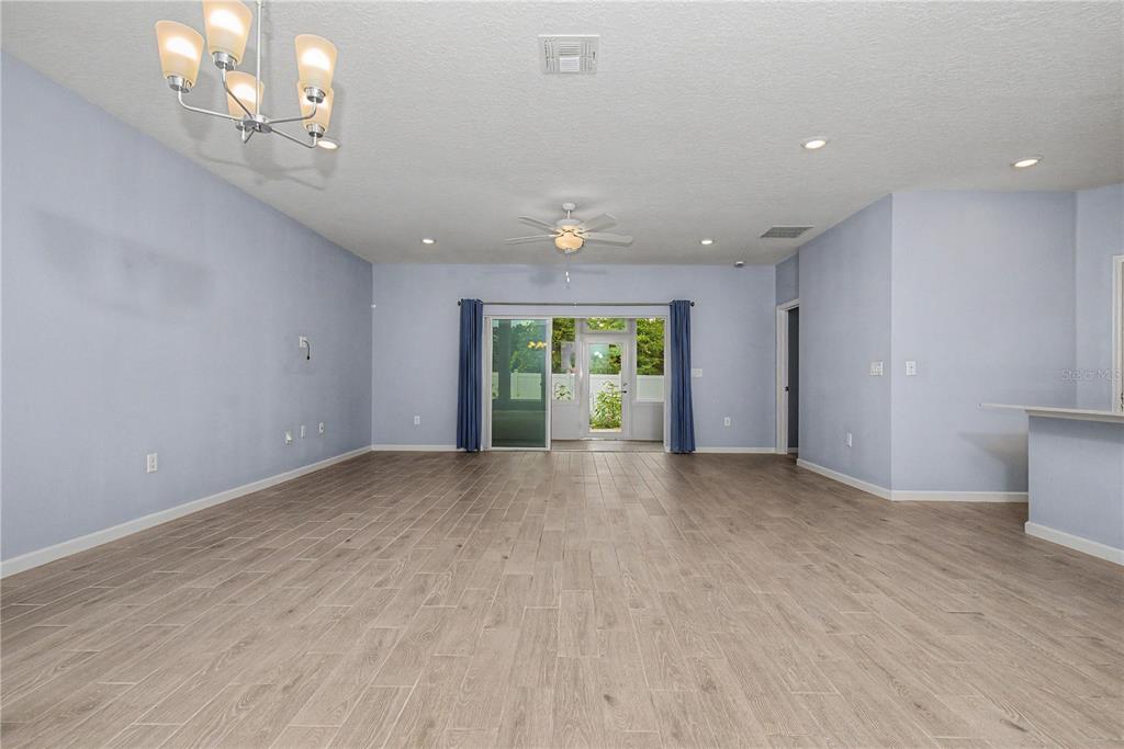 A spacious living room features light blue walls, wood-look tile flooring, and a sliding glass door — 7795 SW 74TH LOOP, OCALA, FL