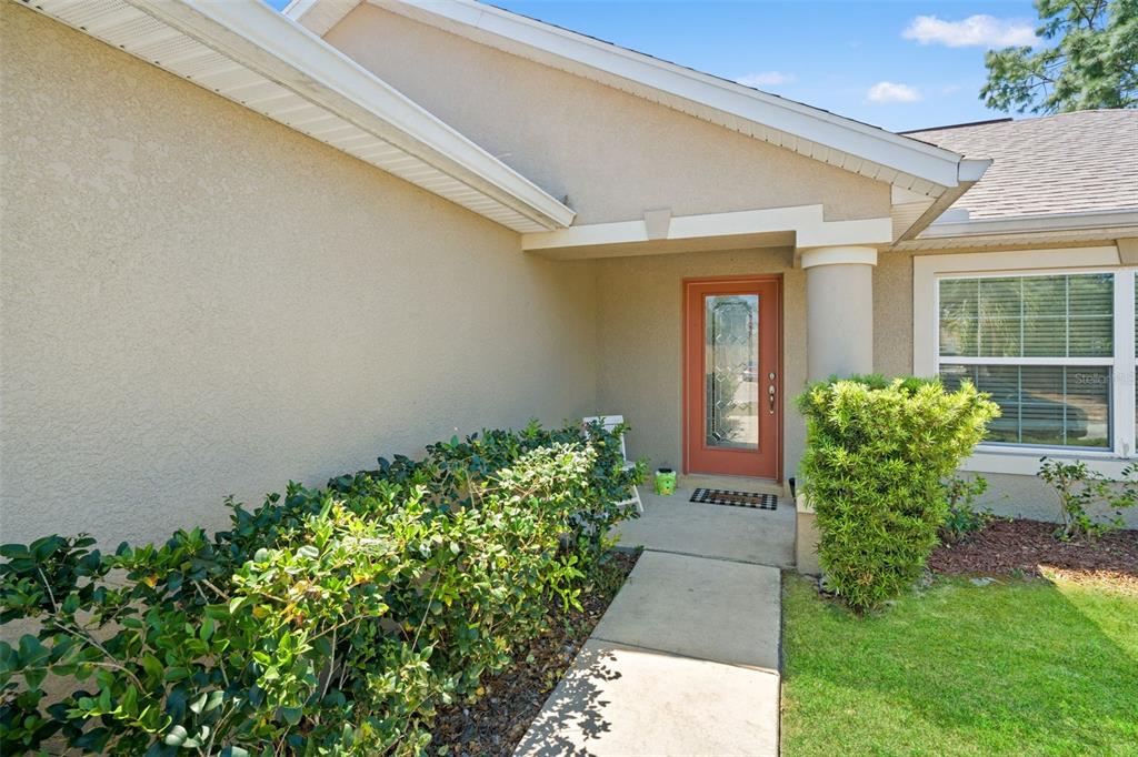 A concrete walkway leads to the front entrance of a house with a red door — 11260 LIBBY ROAD, SPRING HILL, FL