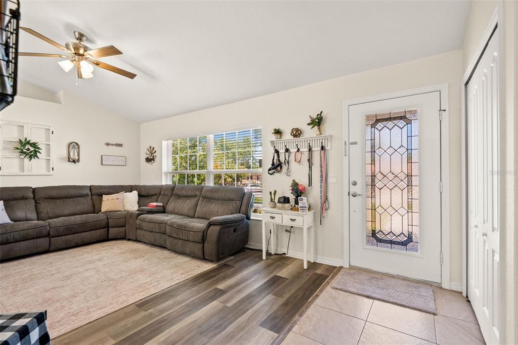 A living room features a grey sectional sofa, wood-look flooring, and a front door with glass — 11260 LIBBY ROAD, SPRING HILL, FL