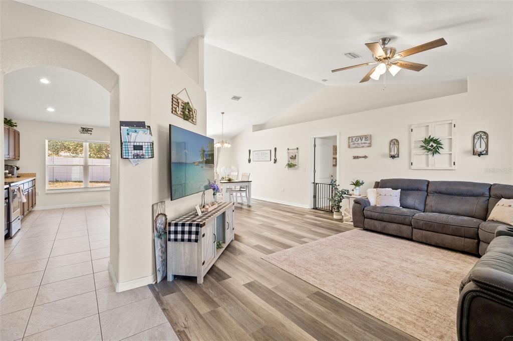 A living room with wood-look flooring, a gray sectional sofa, and an open-concept kitchen — 11260 LIBBY ROAD, SPRING HILL, FL