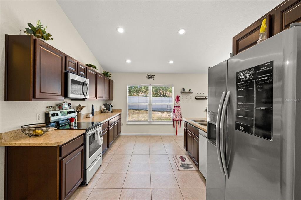 A kitchen features dark wood cabinets, light countertops, stainless steel appliances, and tile flooring — 11260 LIBBY ROAD, SPRING HILL, FL