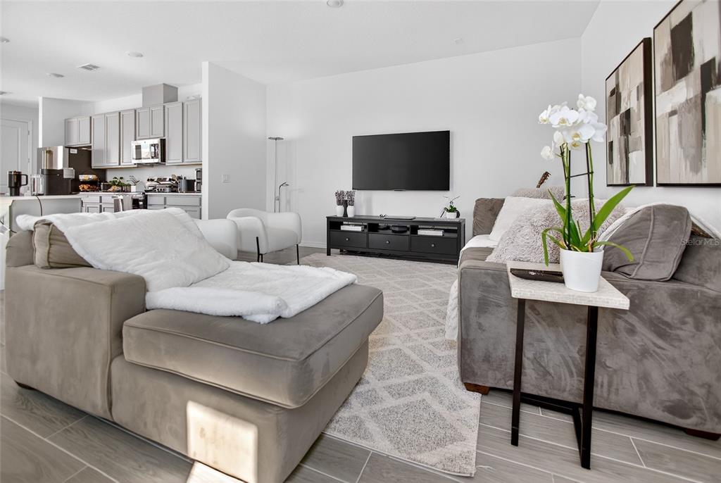 A living room features gray sofas, a television on a black console, and an open kitchen — 17739 SHARP PUMMELO ALLEY, WINTER GARDEN, FL