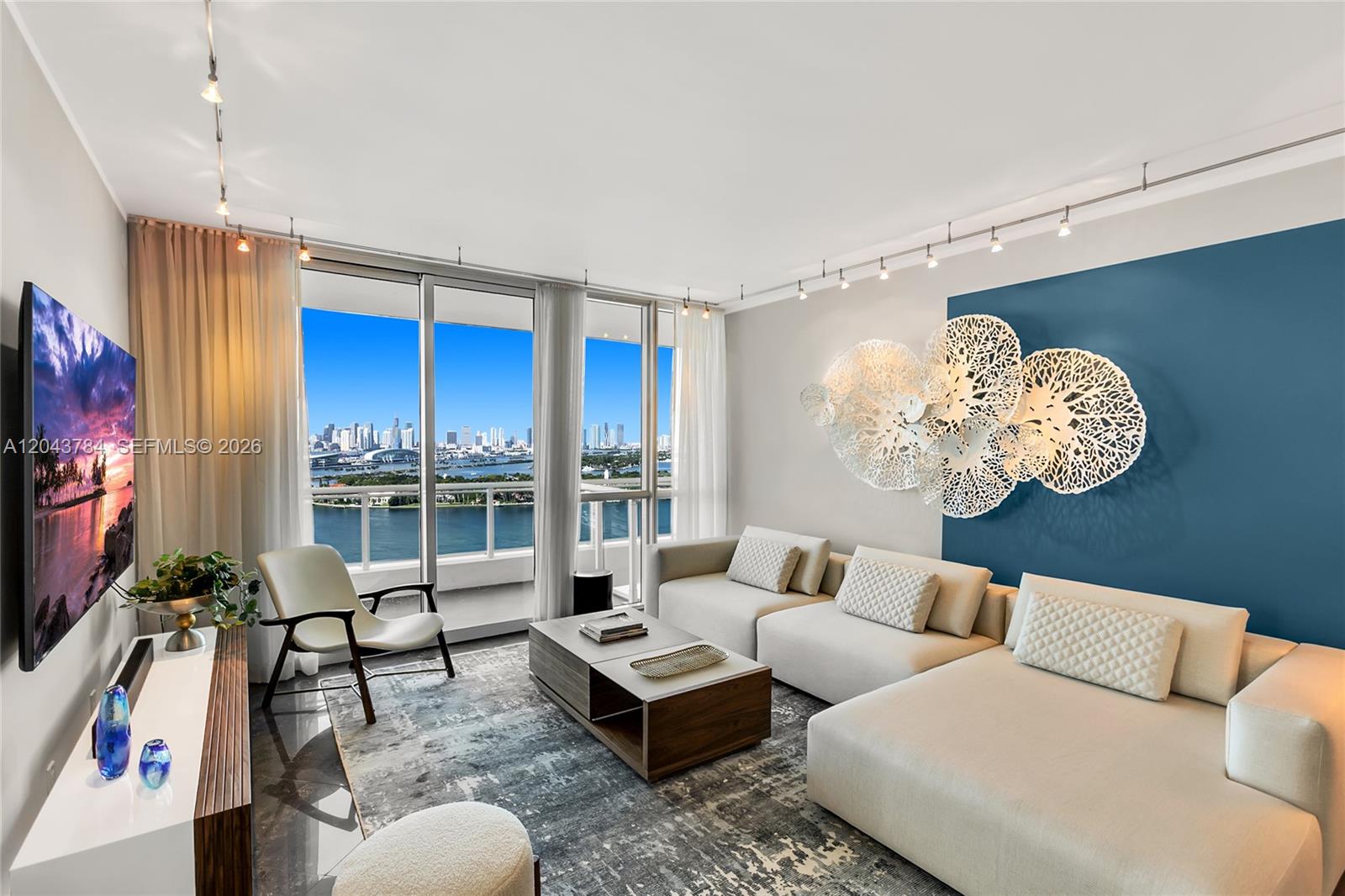 A modern living room features a sectional sofa, blue accent wall, and floor-to-ceiling balcony windows — 540 West Ave # 2311, Miami Beach FL 33139, MIAMI BEACH, FL