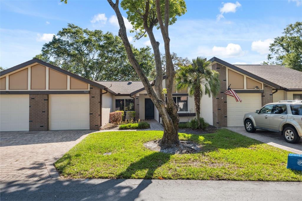 A duplex with brick and stucco siding, two garage doors, and a central tree — 7522 HEATHER WALK DRIVE, WEEKI WACHEE, FL