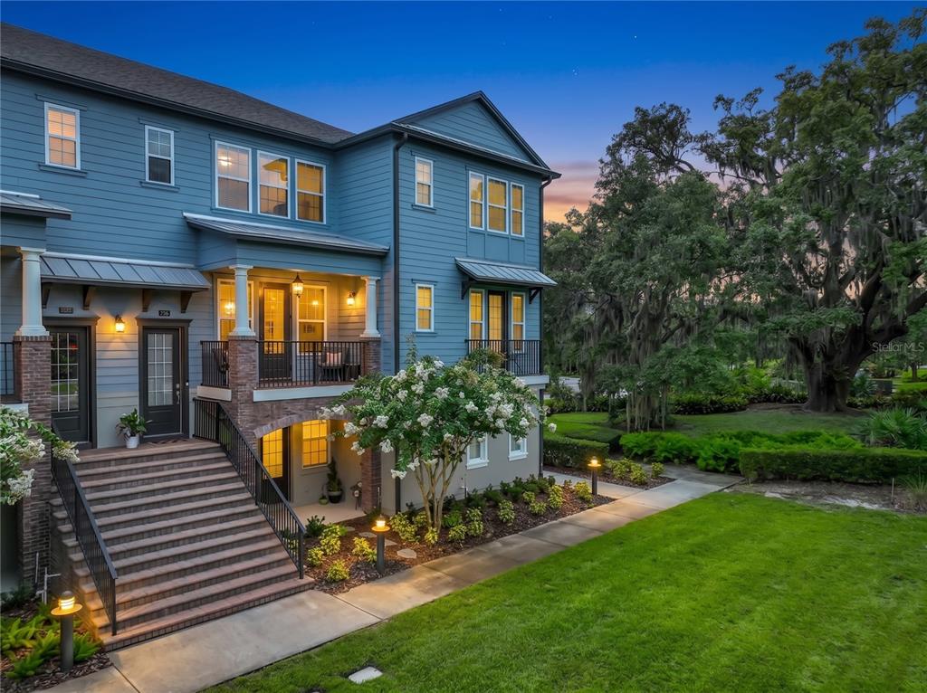 A blue multi-story townhouse features a raised front porch, brick accents, and a landscaped lawn — 736 CATALONIA COVE, OVIEDO, FL