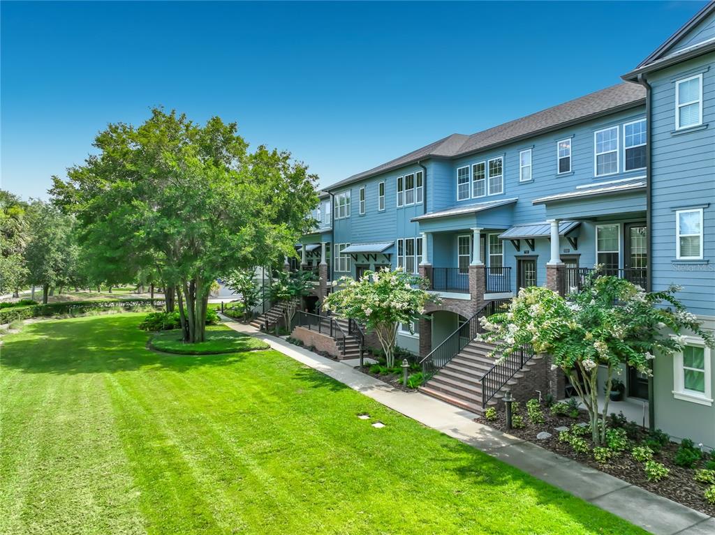 A blue multi-story townhouse exterior with a grassy lawn, trees, and elevated back porches — 736 CATALONIA COVE, OVIEDO, FL