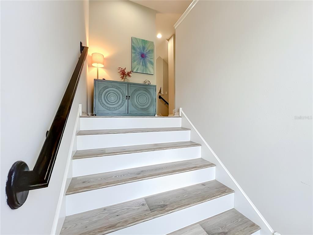 A staircase with wood-look treads and white risers leads to a landing with decor — 736 CATALONIA COVE, OVIEDO, FL