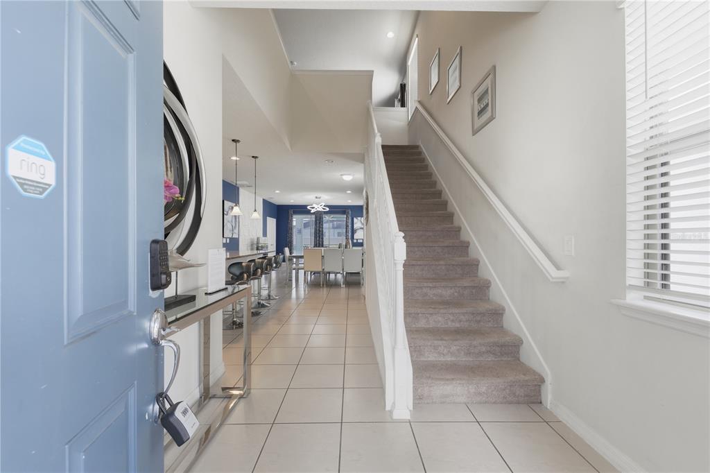 An entryway features a staircase, tiled flooring, and a view into an open-concept dining area — 8956 ZURICH LANE, KISSIMMEE, FL