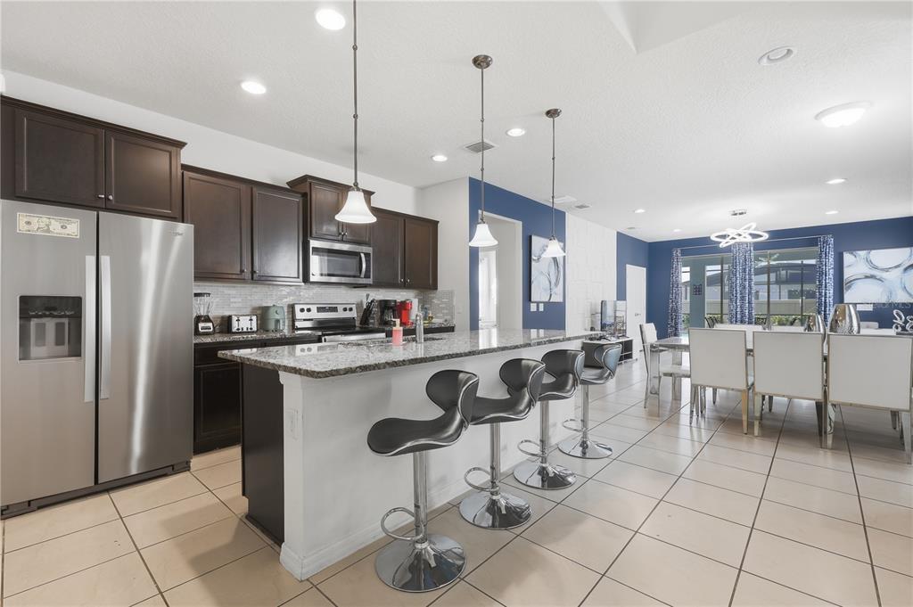 A kitchen features dark wood cabinets, granite countertops, a breakfast bar with stools, and tile flooring — 8956 ZURICH LANE, KISSIMMEE, FL