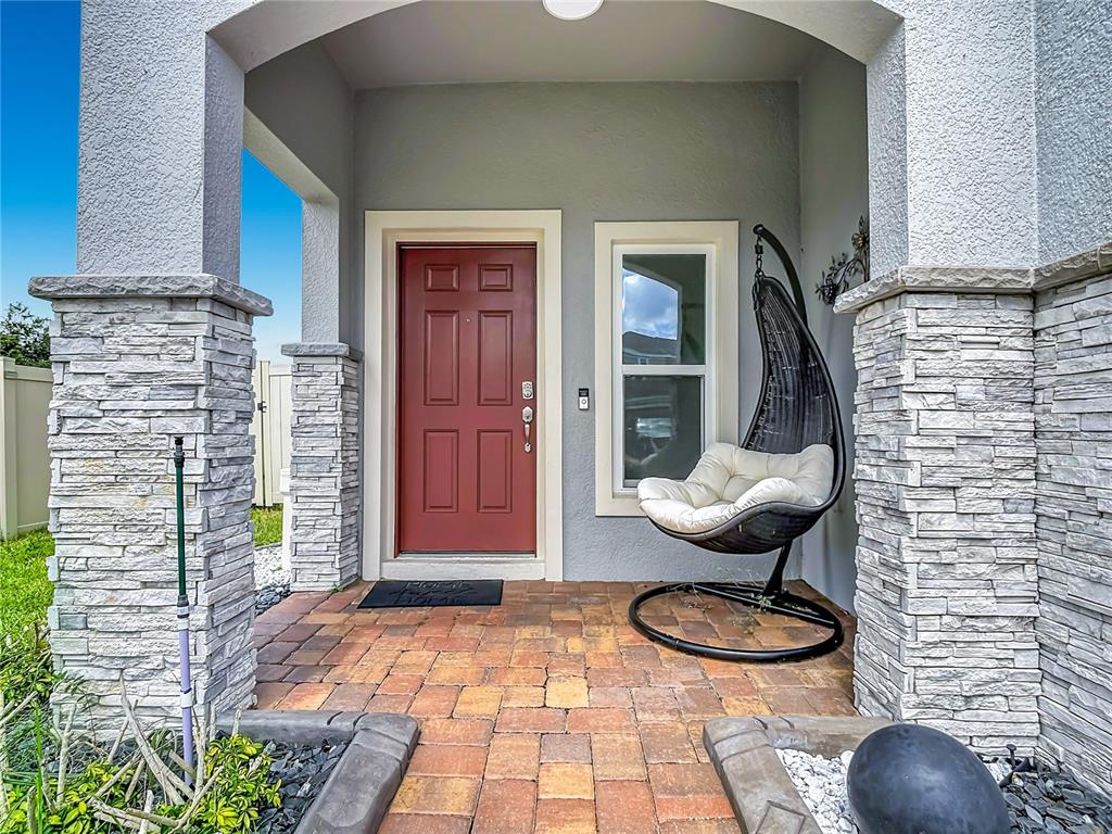 A front porch features a red door, a hanging chair, and stone-clad pillars — 938 ANNA PLACE, DAVENPORT, FL