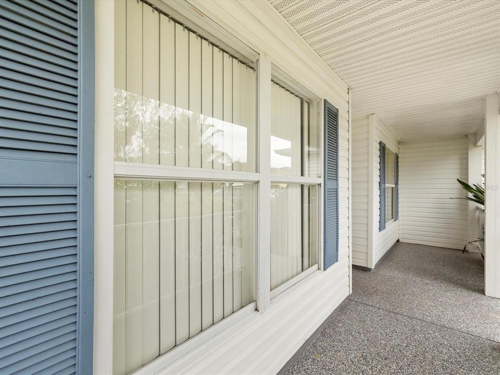 A covered porch features white siding, blue shutters, and a textured concrete floor — 29146 PRINCEVILLE DRIVE, SAN ANTONIO, FL