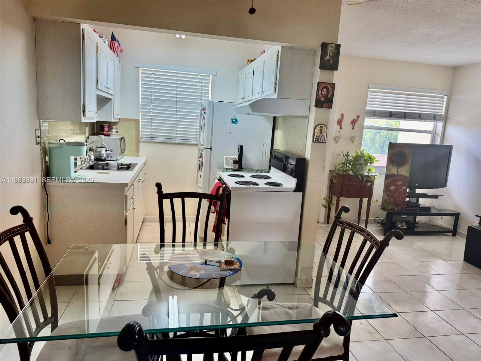 A kitchen with white cabinets and appliances is adjacent to a dining area with a glass table — 2145 Pierce St # 403, Hollywood FL 33020, HOLLYWOOD, FL