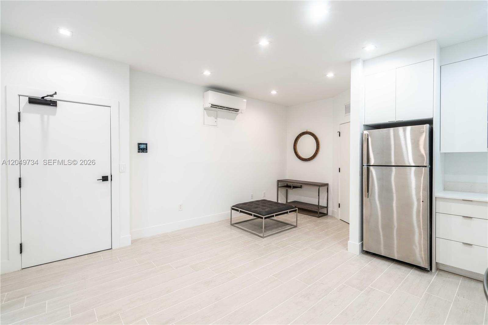 A minimalist room features white walls, light tile flooring, a stainless steel refrigerator, and furniture — 960 Jefferson Ave # 105, Miami Beach FL 33139, MIAMI BEACH, FL