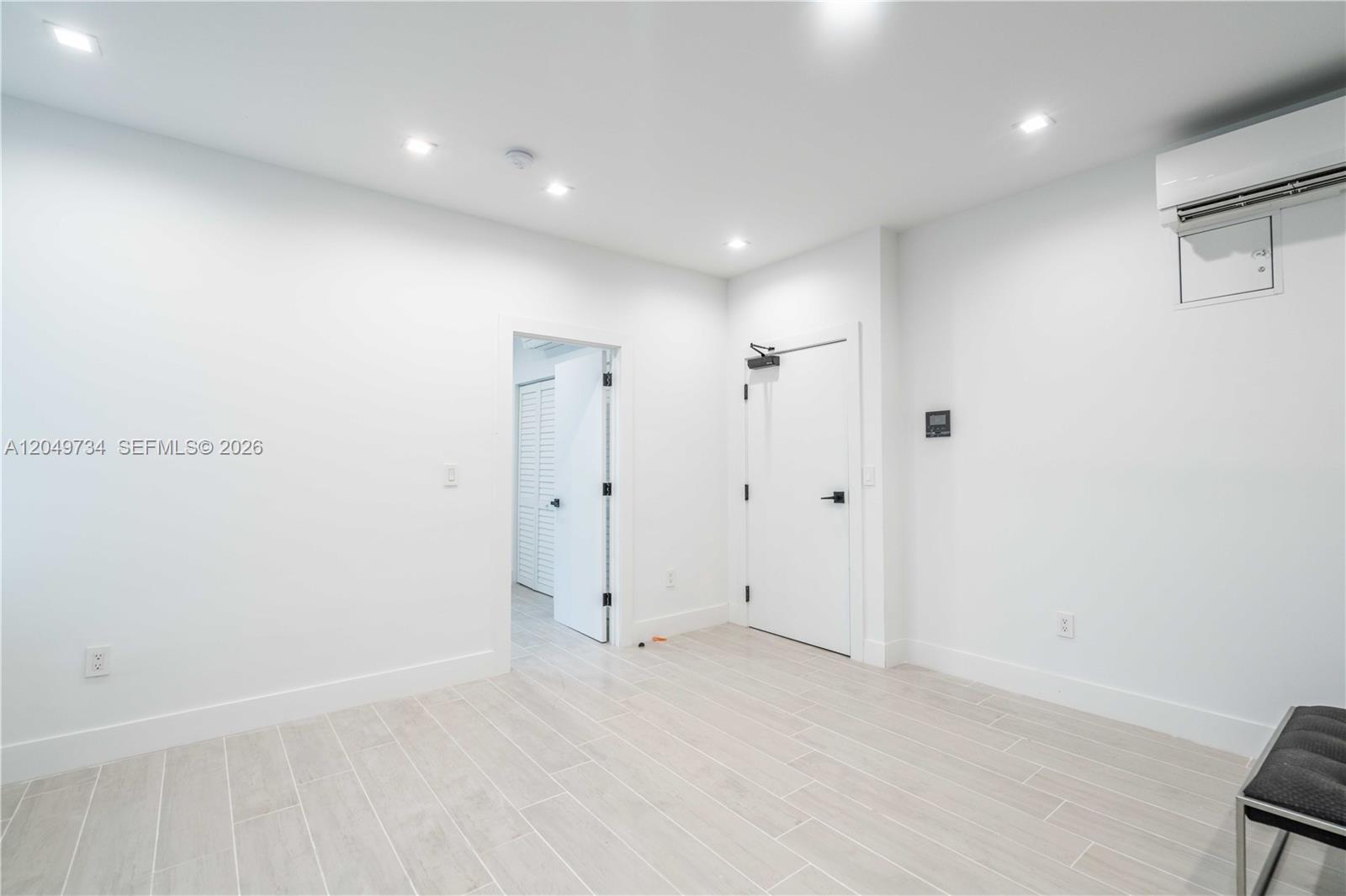 A minimalist room features white walls, light wood-look tile flooring, recessed lighting, and two doors — 960 Jefferson Ave # 105, Miami Beach FL 33139, MIAMI BEACH, FL