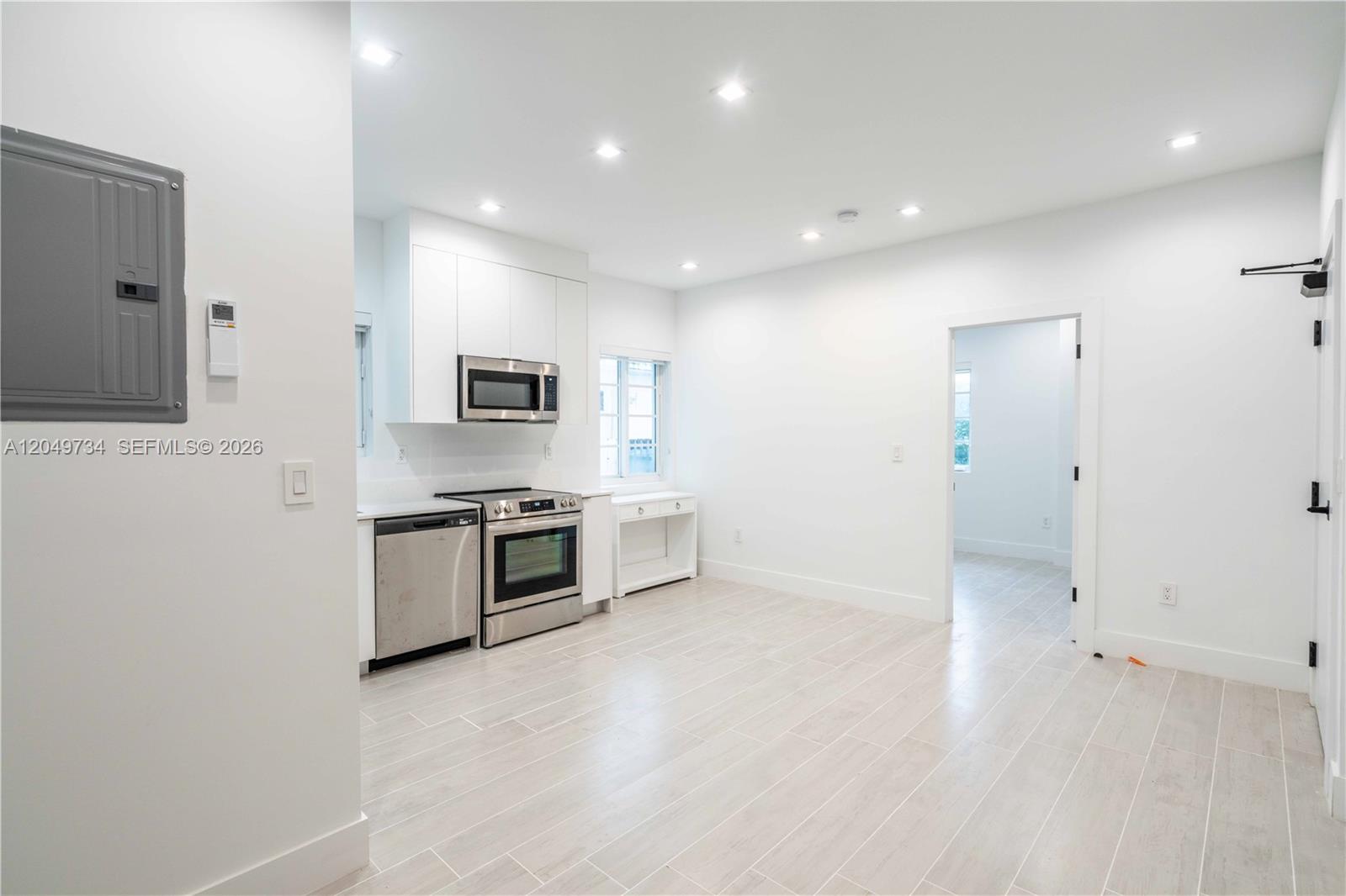 A minimalist kitchen features white cabinetry, stainless steel appliances, and light-colored wood-look tile flooring — 960 Jefferson Ave # 105, Miami Beach FL 33139, MIAMI BEACH, FL