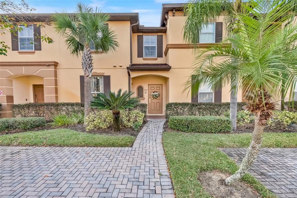 A two-story townhouse exterior features a paved walkway, palm trees, and a tan stucco facade — 237 VERONA AVENUE, DAVENPORT, FL