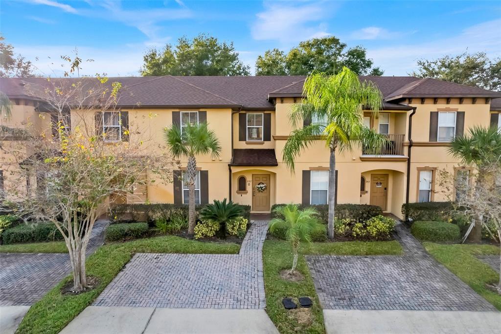 A two-story townhouse exterior with a paved driveway, tan stucco walls, and palm trees — 237 VERONA AVENUE, DAVENPORT, FL