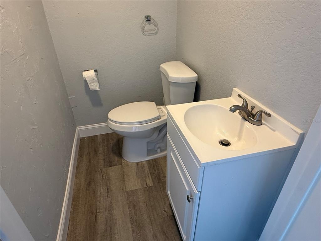 A small bathroom features a white vanity, a toilet, and wood-look flooring — 15 UTILITY DRIVE UNIT A, PALM COAST, FL